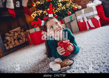 Foto in voller Länge von einem kleinen Mädchen aussehen leer Platz Snacks Kakao tragen grün weihnachtskleidung Tradition Atmosphäre Dekor Haus drinnen Zimmer Stockfoto