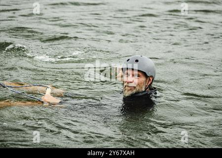 Porträt eines fröhlichen bärtigen Mannes, der während des Wakeboardens auf dem See ins Wasser fällt und in den Kopierraum der Kamera lächelt Stockfoto