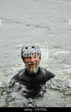 Vertikales Porträt eines fröhlichen bärtigen Mannes, der in den See fällt und Wassersport genießt und in den Kopierraum der Kamera lächelt Stockfoto