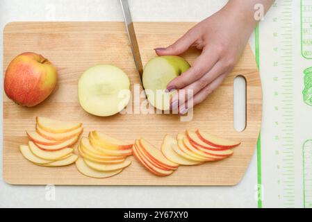 Eine Person, die Äpfel auf einem hölzernen Schneidebrett schneidet, mit einem Messer und einer Hand sichtbar. Geschnittene Äpfel sind ordentlich angeordnet. Kücheneinrichtung. Konzept der Heilung Stockfoto