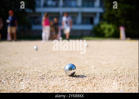 Nahaufnahme von Petanque-Kugeln, die auf Kies verstreut sind, mit dem Zielball im Fokus. Die glänzenden Metallkugeln reflektieren das Sonnenlicht und halten eine verspielte Outdoor-Atmosphäre fest Stockfoto