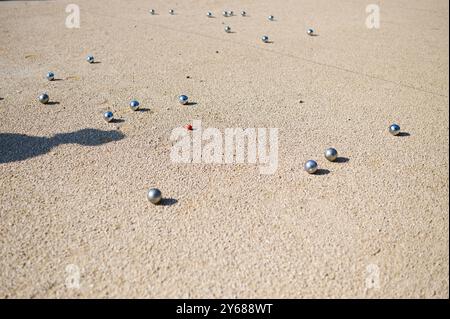 Nahaufnahme von Petanque-Kugeln, die auf Kies verstreut sind, mit dem Zielball im Fokus. Die glänzenden Metallkugeln reflektieren das Sonnenlicht und halten eine verspielte Outdoor-Atmosphäre fest Stockfoto