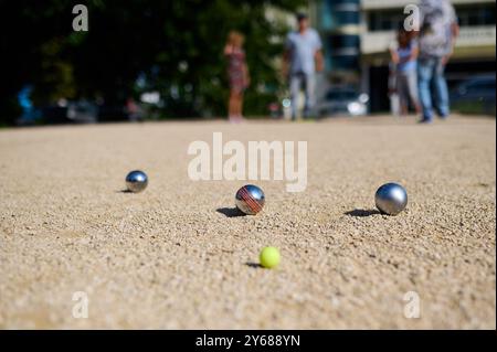 Nahaufnahme von Petanque-Kugeln, die auf Kies verstreut sind, mit dem Zielball im Fokus. Die glänzenden Metallkugeln reflektieren das Sonnenlicht und halten eine verspielte Outdoor-Atmosphäre fest Stockfoto