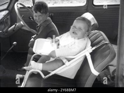 1950er Jahre, historisch, kleiner Junge sitzt auf dem Fahrersitz von Dads Auto, kleiner Bruder nebenan auf dem Autositz?? Der Ära mit Tablett??? Stockfoto