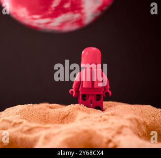 Rote Astronautenfigur, die auf Sand auf einem Planeten steht und einen anderen roten Planeten ansieht. Rückansicht. Stockfoto