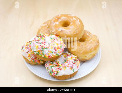 Weißer Porzellanteller mit glasierten und mattierten Tortenkrapfen mit Streuseln auf einem hellen Holztisch. Stockfoto