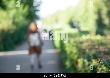 Verschwommener Hintergrund, anonyme junge Frau, die die Straße im Park entlang läuft. Sonniger Sommertag, Stockfoto