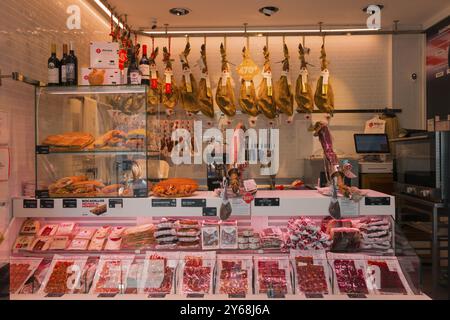 Moderne Metzgerei mit Fleischtheke, hängenden Schinken, Würstchen und Weinflaschen, beleuchtet und ordentlich eingerichtet, Nerja, Provinz Mala Stockfoto