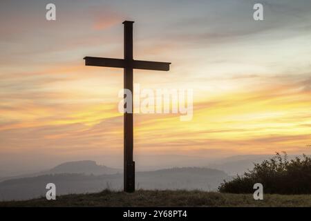 Ein Kreuz steht vor einem farbenfrohen Sonnenuntergangshimmel auf einem Hügel und schafft eine ruhige und spirituelle Atmosphäre, Bisberg, Watterdingen, Hegau, Bodensee Re Stockfoto