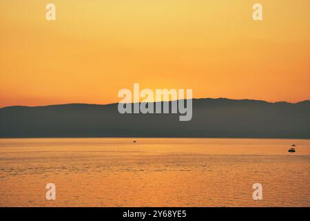 Goldener Sonnenuntergang über den Gewässern des Ohrid-Sees, Mazedonien. Boote mit Touristen befahren das Wasser des Sees. Ein Berg in der Ferne. Stockfoto