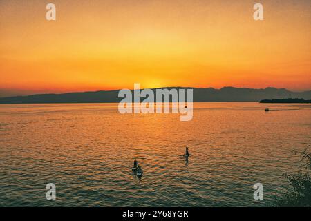 Goldener Sonnenuntergang über den Gewässern des Ohrid-Sees, Mazedonien. Boote mit Touristen befahren das Wasser des Sees. Ein Berg in der Ferne. Stockfoto