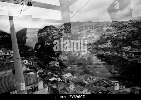 Reflektionen und Schatten verschmelzen mit den Häusern am Hügel in einem faszinierenden Blick von der Seilbahn, während eine andere vorbeifährt Stockfoto