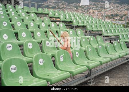 Blondes Kind erkundet leere Stadionsitze, in der Hand, vor dem Hintergrund der Stadt Funchal am Hügel Stockfoto