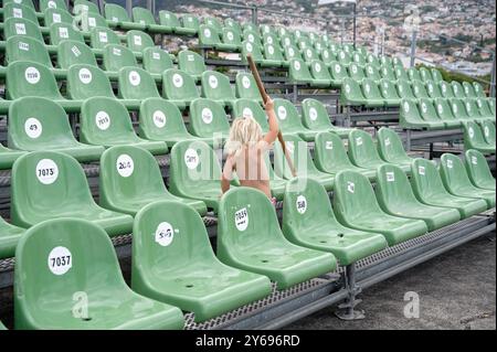 Blondes Kind erkundet leere Stadionsitze, in der Hand, vor dem Hintergrund der Stadt Funchal am Hügel Stockfoto