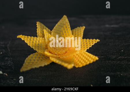 Eine einzelne, handgefertigte Kerze mit Wabenmuster sitzt auf einem dunklen Holztisch. Die Kerze ist wie eine Blume geformt, mit einer zentralen Blüte und zarten Blütenblättern. Stockfoto