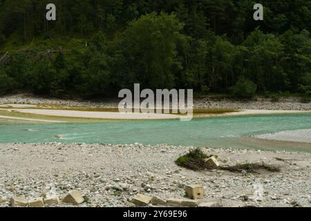 Klares türkisfarbenes Wasser fließt sanft um goldene Sandbänke, flankiert von glatten Steinen und leuchtend grünem Laub, die ein Gefühl der Ruhe und Verbundenheit einladen Stockfoto