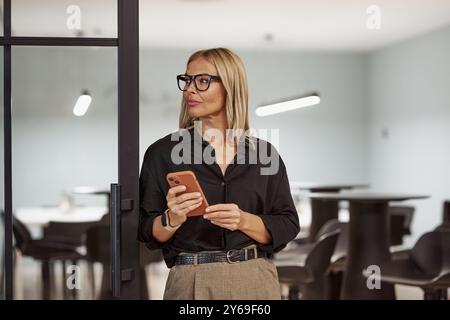 Eine selbstbewusste Geschäftsfrau kommuniziert per Smartphone in einem modernen Büro und zeigt Führungsqualitäten Stockfoto
