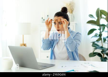 Schockierte aufgeregte Frau arabischer oder indischer Nationalität mit Brille, Büroangestellte, schaut auf den Laptop-Bildschirm in einer überraschenden Brille, sah unerwartete Informationen im Internet Stockfoto