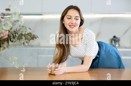Die Hausfrau lehnt sich die Ellbogen auf den Tisch und hält eine Glasschale mit Cappuccino und Kaffee in den Palmen Stockfoto