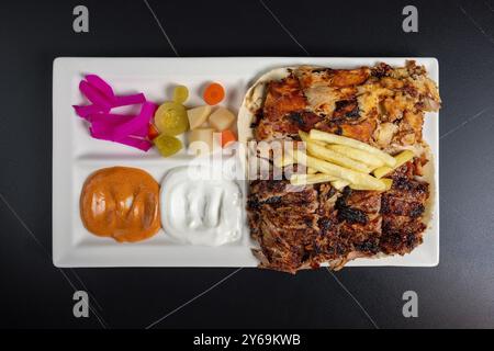 Shawarma-Teller mit Huhn und Rindfleisch, serviert mit Pommes frites, Gurken und Saucen, türkischem Döner Kebab auf einem Teller Stockfoto