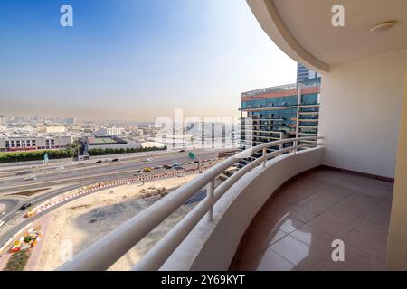 Blick von einem hohen Balkon in Dubai mit Fliesenboden. Darunter befindet sich eine geschäftige Autobahn und ein modernes Hochhaus mit Glasfenstern. Klarer, sonniger Himmel Stockfoto