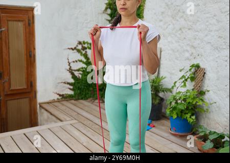 Eine Frau führt auf einer hölzernen Terrasse Widerstandsübungen durch. Sie trägt sportliche Kleidung und konzentriert sich auf Outdoor-Fitness in einer ruhigen Umgebung. Stockfoto