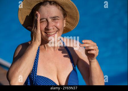 Porträt einer älteren Frau, die im Urlaub Sonnencreme auf ihr Gesicht aufträgt. Stockfoto