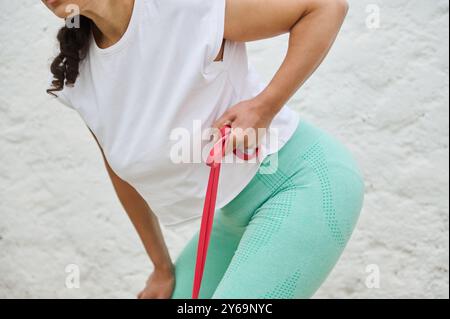 Nahaufnahme einer Frau mit Widerstandsband zur Ausübung der Armmuskulatur. Sie trägt sportliche Kleidung im Freien und betont dabei Fitness und Kraft Stockfoto