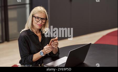 Eine professionelle Frau, die aktiv mit ihrem Laptop und Smartphone in einer Büroumgebung arbeitet Stockfoto
