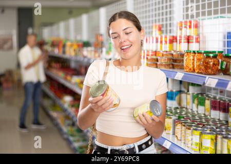 Eine junge Frau, die Konserven im Laden auswählt Stockfoto