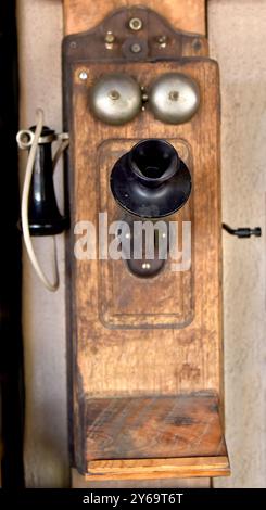 Antikes, wandkurbeliges Telefon hängt an einer lehmwand in New Mexico. Die Metallkurbel befindet sich an der Seite des Telefons. Stockfoto