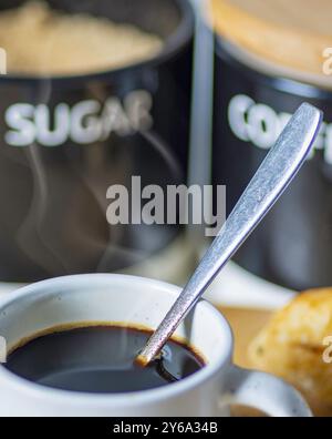 Heißer Espresso-Kaffee, in einer kleinen, weißen Tasse, mit einem Teelöffel innen, kurz nach dem Rühren, Worcestershire, Großbritannien. Stockfoto