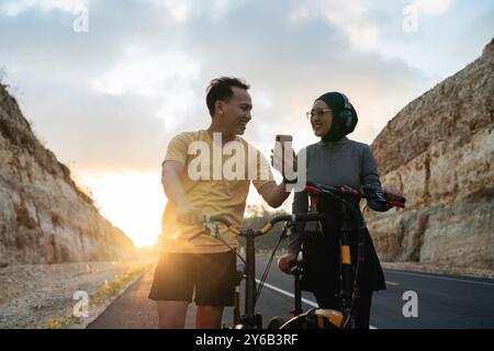 Männliche Radfahrer und Paare benutzen Telefon, wenn sie während des Sonnenuntergangs Radfahren Stockfoto