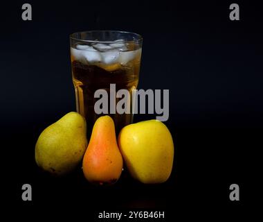 Mischung aus Birnen-Apfel-Saft mit Eis in einem hohen Glas und Reifen Früchten verschiedener Sorten auf schwarzem Hintergrund. Nahaufnahme. Stockfoto