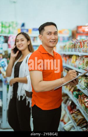 Ein männlicher Arbeiter lächelt in die Kamera, während er im Supermarkt mit Klemmbrett steht Stockfoto