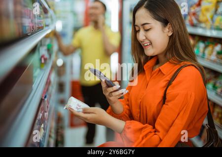 Junge Frau, die Einkaufsartikel hält und mit dem Handy fotografiert hat Stockfoto