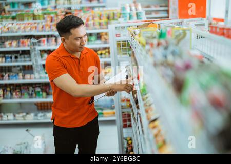 Männlicher Verkäufer, der vor einem Regal steht und Preise überprüft Stockfoto