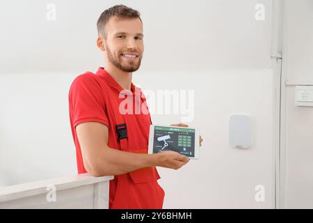 Männlicher Arbeiter, der einen Tablet-Computer mit installiertem Alarmsystem im Zimmer hält Stockfoto