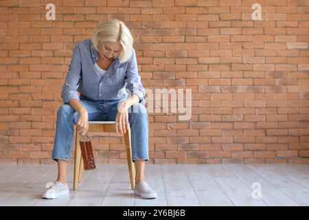 Betrunkene, reife Frau mit Whiskey, die auf einem Stuhl in der Nähe einer Ziegelmauer sitzt. Der Begriff des Alkoholismus Stockfoto