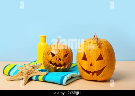 Halloween-Kürbisse mit Seesternen, Sonnencreme und Handtuch auf blauem Hintergrund Stockfoto