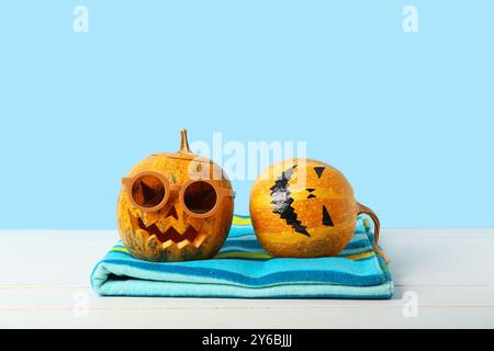 Halloween Kürbisse mit Sonnenbrille und Handtuch auf blauem Hintergrund Stockfoto