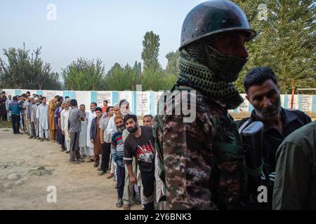 Indischer paramilitärischer Soldat steht auf der Wache, während die kaschmirischen Wähler in der zweiten Phase der Parlamentswahlen in Jammu und Kaschmir am Stadtrand von Srinagar in einer Warteschlange warten, um ihre Stimmzettel vor dem Wahlhaus abzugeben. Dies sind die ersten Kommunalwahlen seit einem Jahrzehnt und die ersten, seit Neu-Delhi 2019 den halbautonomen Status der Region widerrief und sie unter direkte Herrschaft stellte. Fast neun Millionen Menschen sind registriert, um in der umstrittenen Region zu wählen, die traditionell für Boykotte aus Protest gegen die indische Herrschaft bekannt ist. Stockfoto