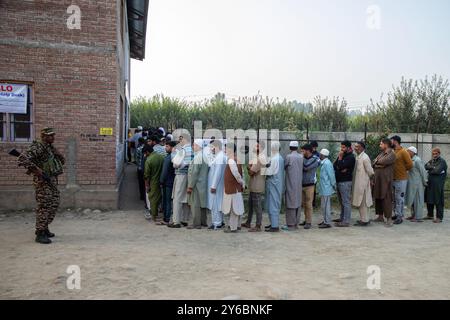 Indischer paramilitärischer Soldat steht auf der Wache, während die kaschmirischen Wähler in der zweiten Phase der Parlamentswahlen in Jammu und Kaschmir am Stadtrand von Srinagar in einer Warteschlange warten, um ihre Stimmzettel vor dem Wahlhaus abzugeben. Dies sind die ersten Kommunalwahlen seit einem Jahrzehnt und die ersten, seit Neu-Delhi 2019 den halbautonomen Status der Region widerrief und sie unter direkte Herrschaft stellte. Fast neun Millionen Menschen sind registriert, um in der umstrittenen Region zu wählen, die traditionell für Boykotte aus Protest gegen die indische Herrschaft bekannt ist. Stockfoto