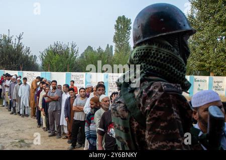 Indischer paramilitärischer Soldat steht auf der Wache, während die kaschmirischen Wähler in der zweiten Phase der Parlamentswahlen in Jammu und Kaschmir am Stadtrand von Srinagar in einer Warteschlange warten, um ihre Stimmzettel vor dem Wahlhaus abzugeben. Dies sind die ersten Kommunalwahlen seit einem Jahrzehnt und die ersten, seit Neu-Delhi 2019 den halbautonomen Status der Region widerrief und sie unter direkte Herrschaft stellte. Fast neun Millionen Menschen sind registriert, um in der umstrittenen Region zu wählen, die traditionell für Boykotte aus Protest gegen die indische Herrschaft bekannt ist. Stockfoto