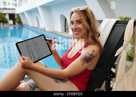 Lächelnde Frau, Die Tablet Hält, Während Sie Am Pool Sitzt Stockfoto