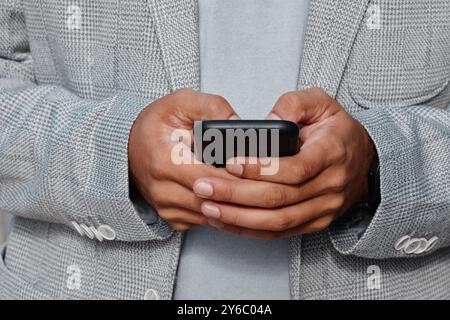 Nahaufnahme eines Mannes, der einen grauen Blazer trägt, während er das Smartphone in der Hand hält und den Fokus auf Technologie und Verbindung zeigt, ohne das Gesicht zu enthüllen Stockfoto