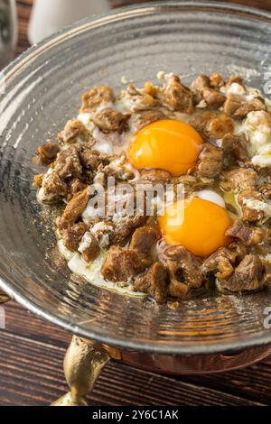 Eier mit Fleisch, gebraten in einer Kupferpfanne auf einem Holztisch. Türkischer Name kavurmali yumurta Stockfoto