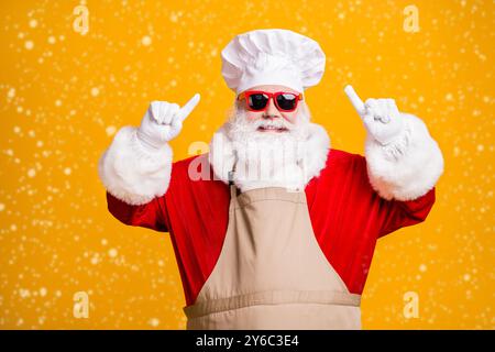 Foto von santa claus mit Bart Point Finger seinem Koch Kochen Hut x-Mas weihnachten noel Fest Vorbereitung tragen Schürze Sonnenglas Isoliert über hell Stockfoto