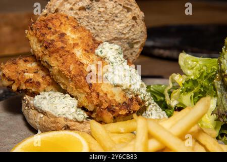 Ein köstlicher Teller mit geräuchertem Haddock Fish Finger Sandwich mit Pommes und Tartarsauce auf einem hölzernen Küchentisch Stockfoto