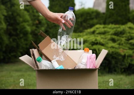 Recyclingkonzept. Frau, die Plastikflasche draußen in den Karton steckt, Nahaufnahme Stockfoto